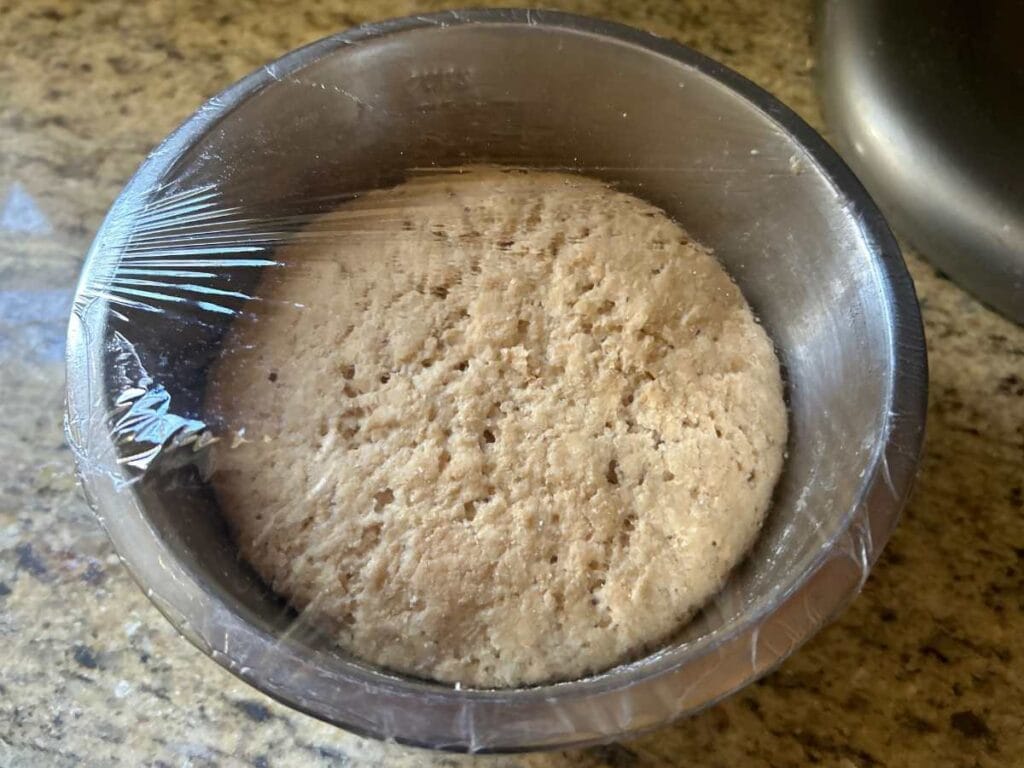 biga preferment in a metal bowl with plastic wrap