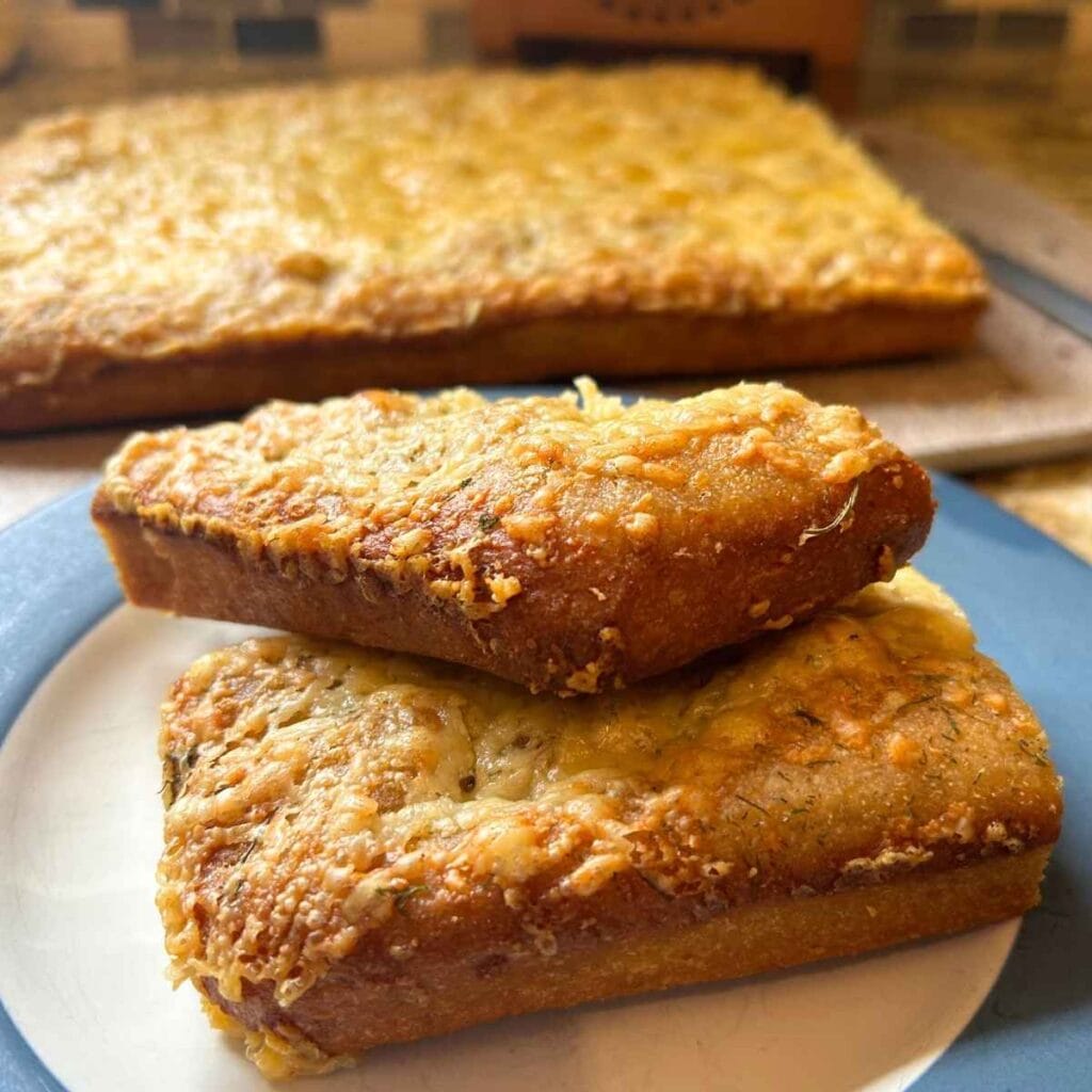 two slices of cheesy sourdough focaccia bread stacked on a plate in front of the loaf