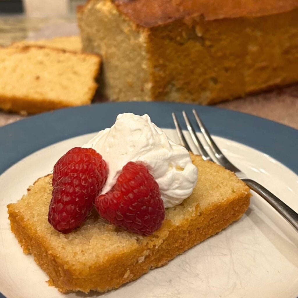 a slice of sourdough pound cake on a plate topped with whipped cream and raspberries