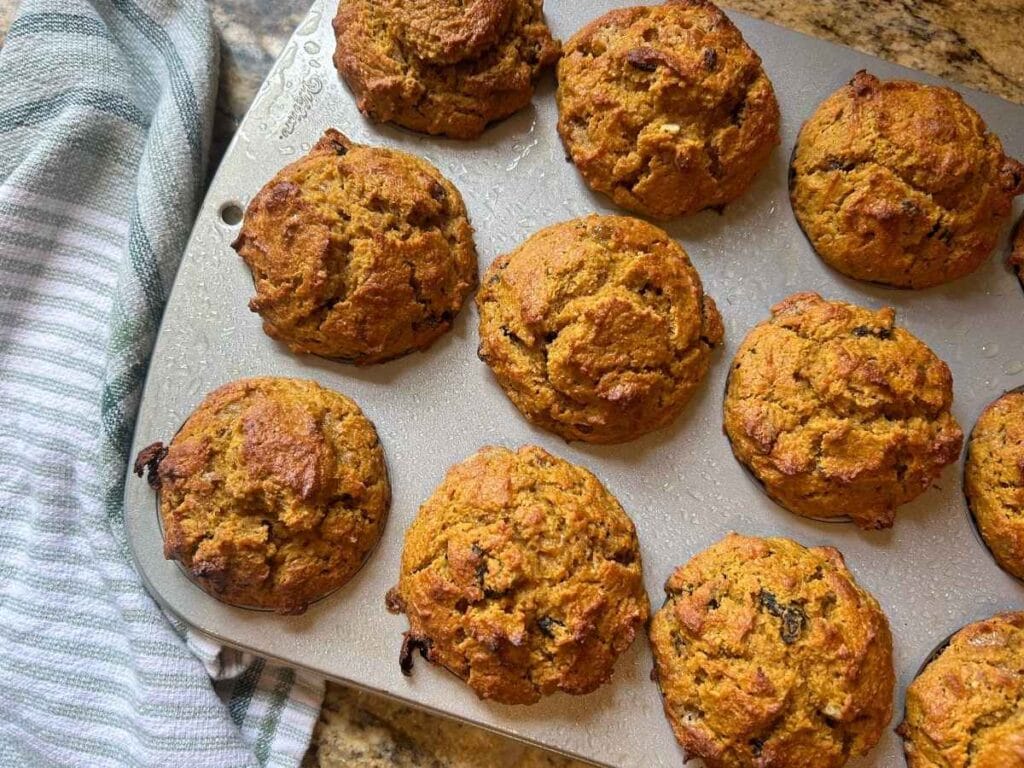 baking pumpkin raisin pecan muffins in a muffin tine next to a green striped towel.