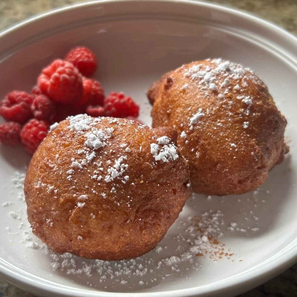 two Italian zeppole and raspberries on a white place sprinkled with powdered sugar