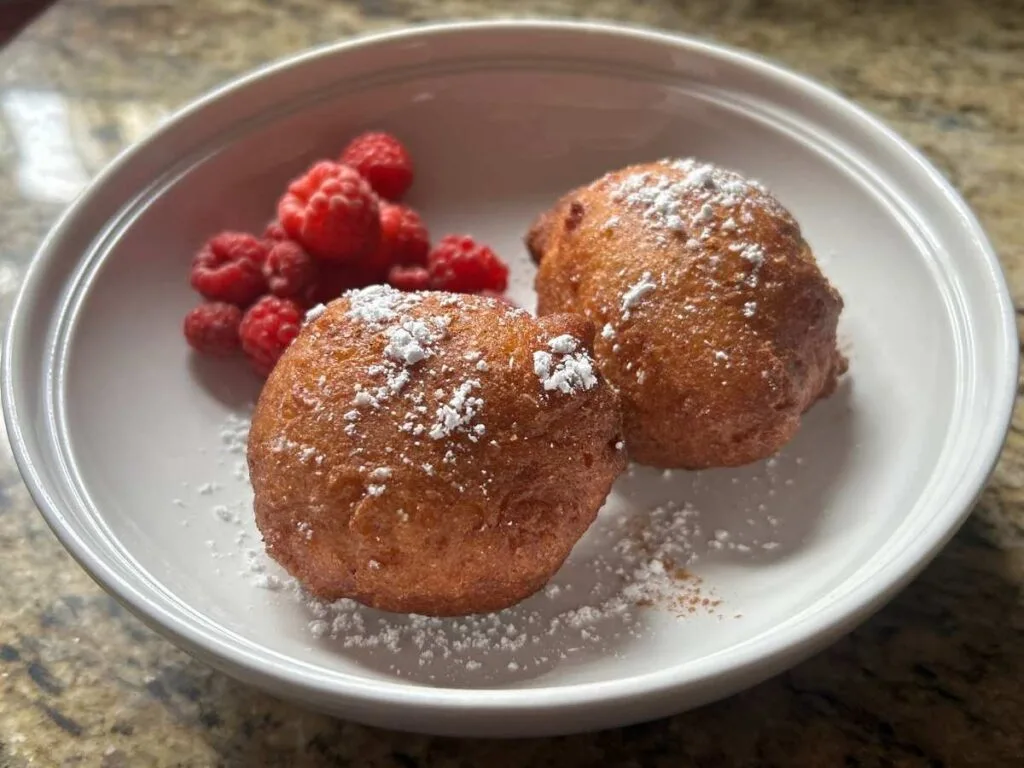 two Italian zeppole and raspberries on a white place sprinkled with powdered sugar