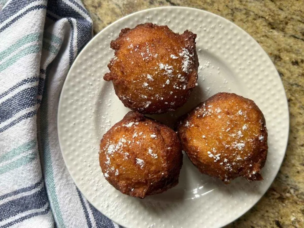 three fried donut balls on a white place sprinkled with powdered sugar