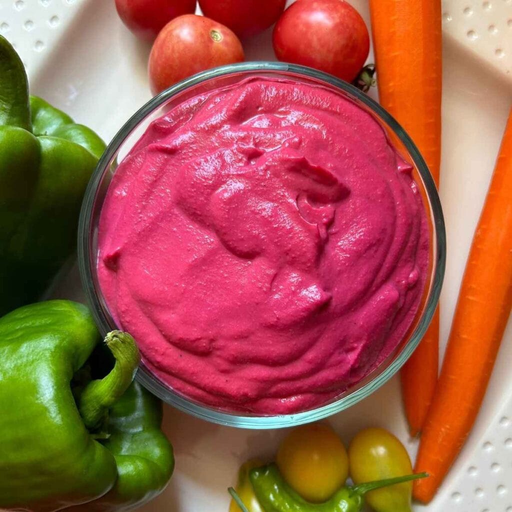 beet hummus on a white tray surrounded by vegetables