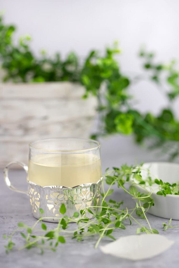 metallic and glass mug full of thyme simple syrup and thyme sprigs surrounding it