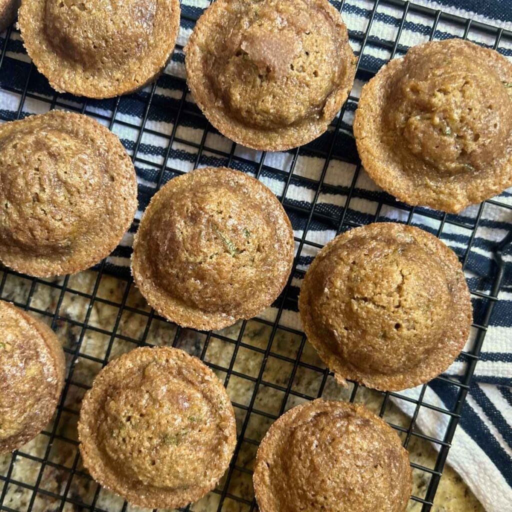 top view of zucchini muffins on a wire rack over a blue and white striped towel