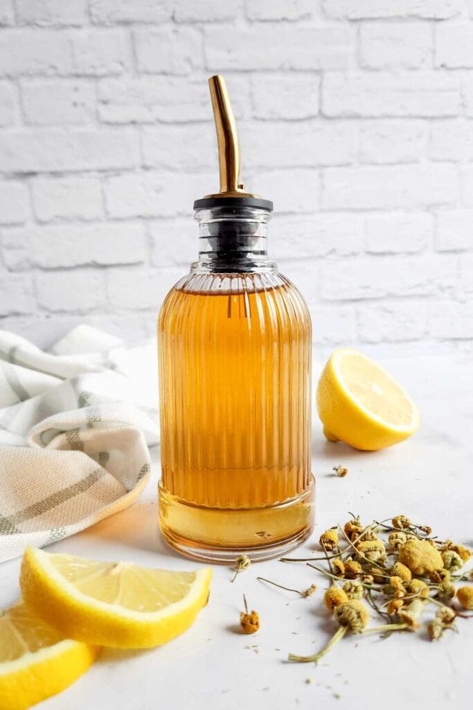 bottle of chamomile simple syrup next to flower buds