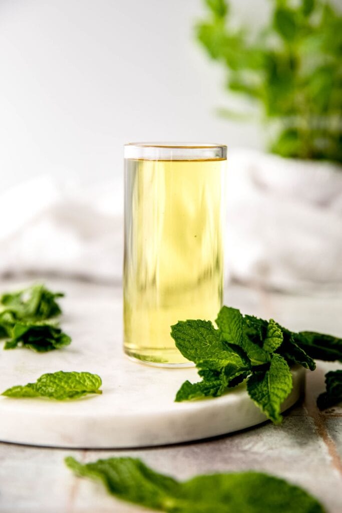 large glass of mint simple syrup surrounded by mint leaves