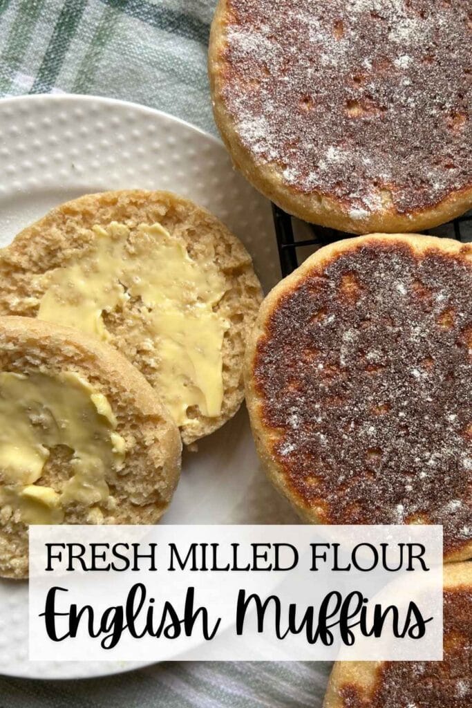 close up of English muffins on a cooling rack next to a split and buttered one on a white plate for pinterest image