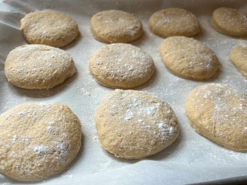 cut english muffin dough on parchment paper on a baking sheet