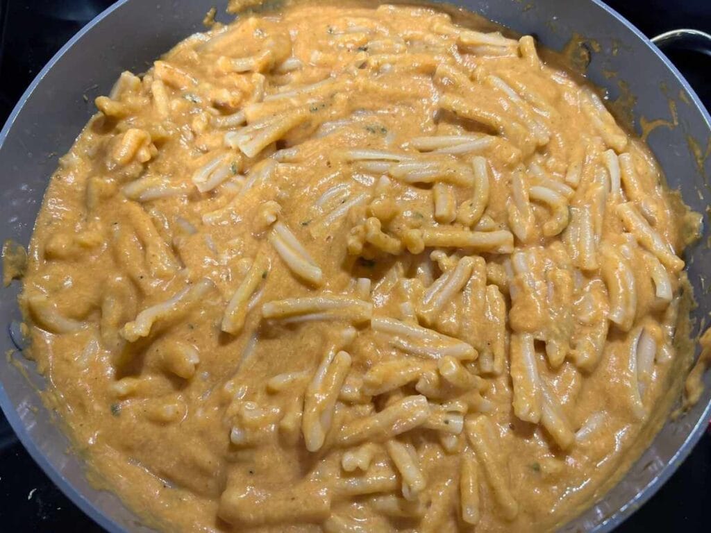 skillet full of pumpkin cheese sauce mixed with noodles