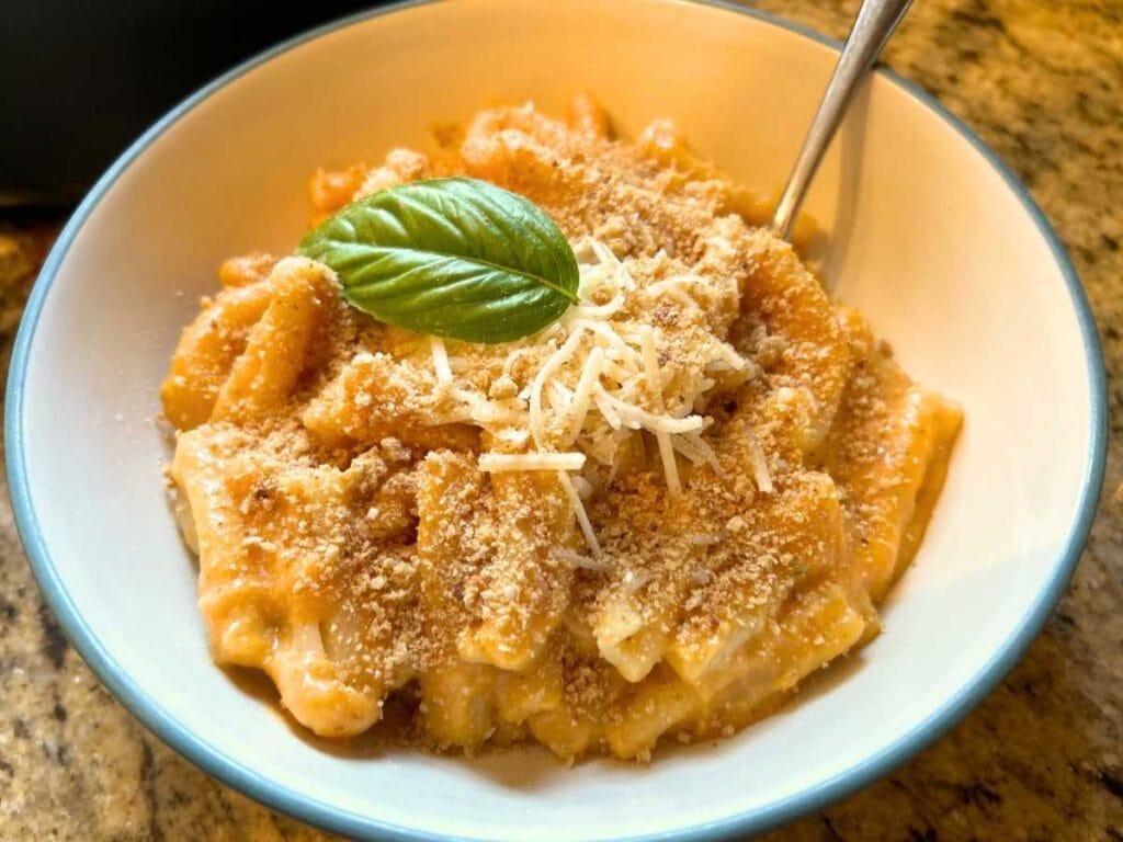 bowl of pumpkin mac and cheese topped with sourdough breadcrumbs, cheese, and basil