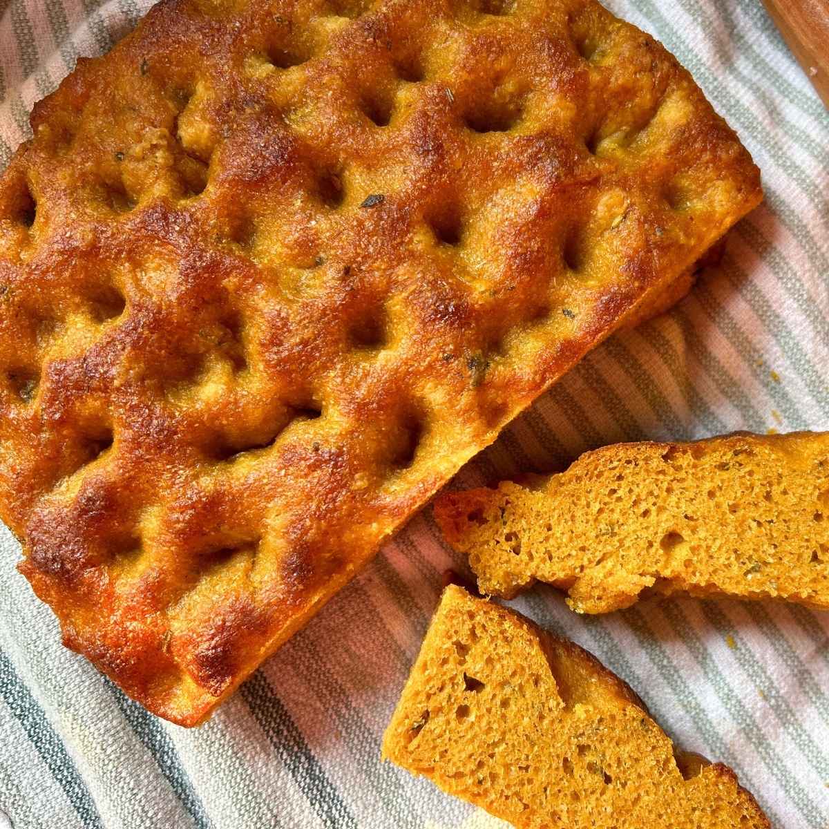 round loaf of sourdough pumpkin and herb focaccia on green and white striped towel