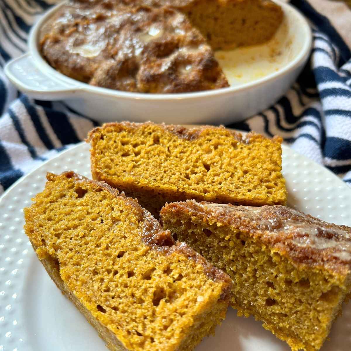 three slices of pumpkin pie focaccia on a white plate in front of the baking pan with the rest of the loaf on a navy and white striped towel