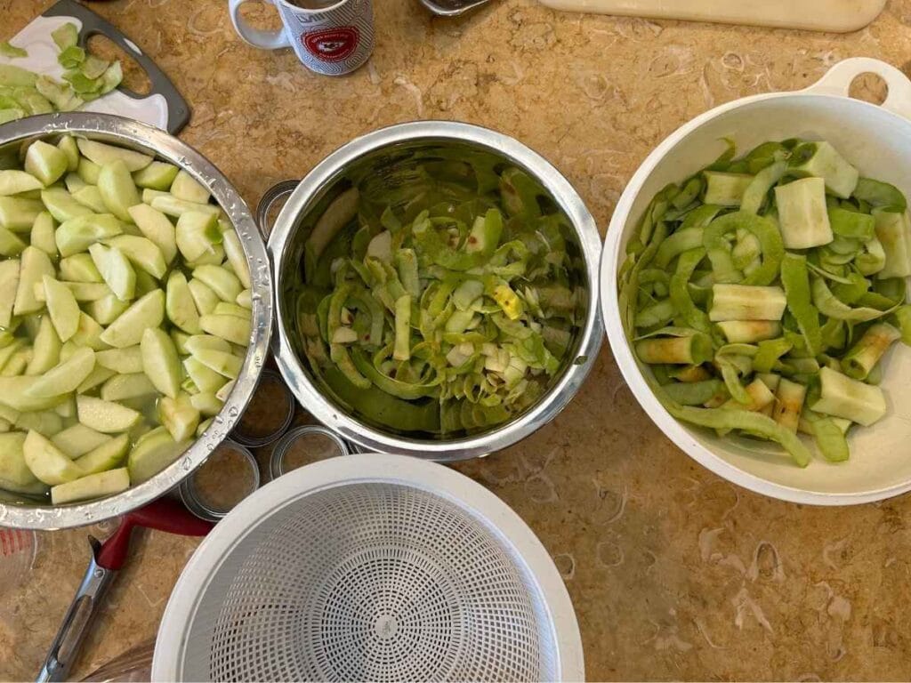 sliced apples in a bowl next to peels in a bowl and cores in a bowl
