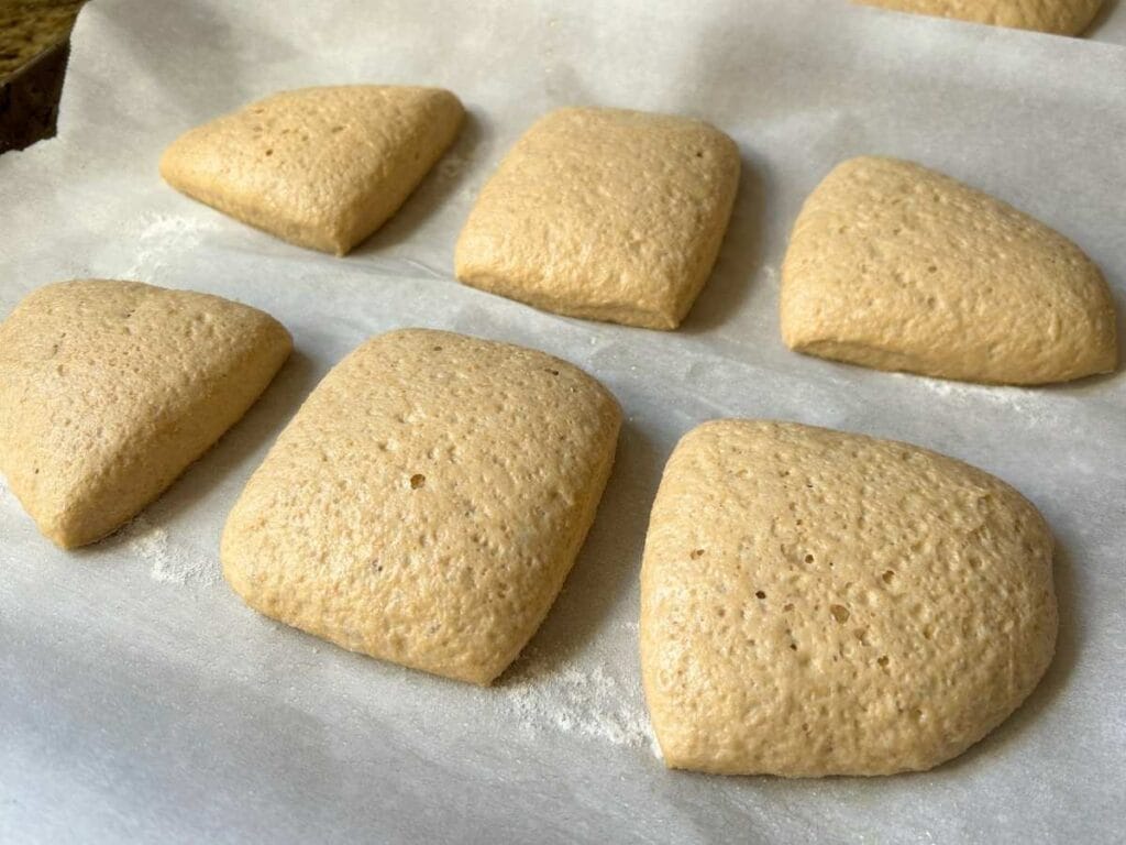 six pre-baked ciabatta rolls on parchment paper after rising