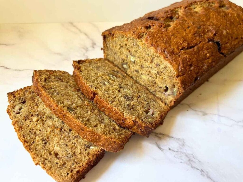 three slices cut off of a loaf of banana bread and laid in front of it