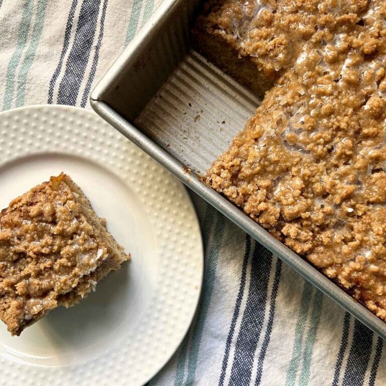 top view of a slice of coffee cake on a white plate next to the pan with the rest of the cake