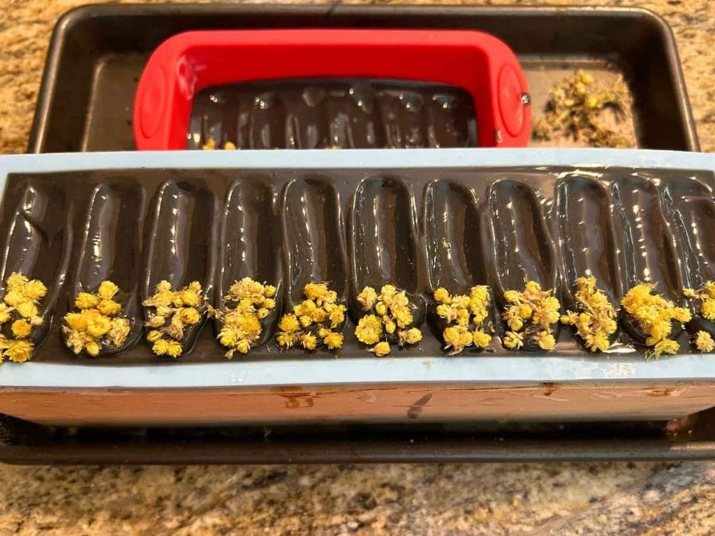 charcoal and tea tree tallow soap in molds topped with yellow flowers