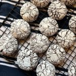 sourdough chocolate crinkle cookies on a cooking rack on top of a navy and white striped towel