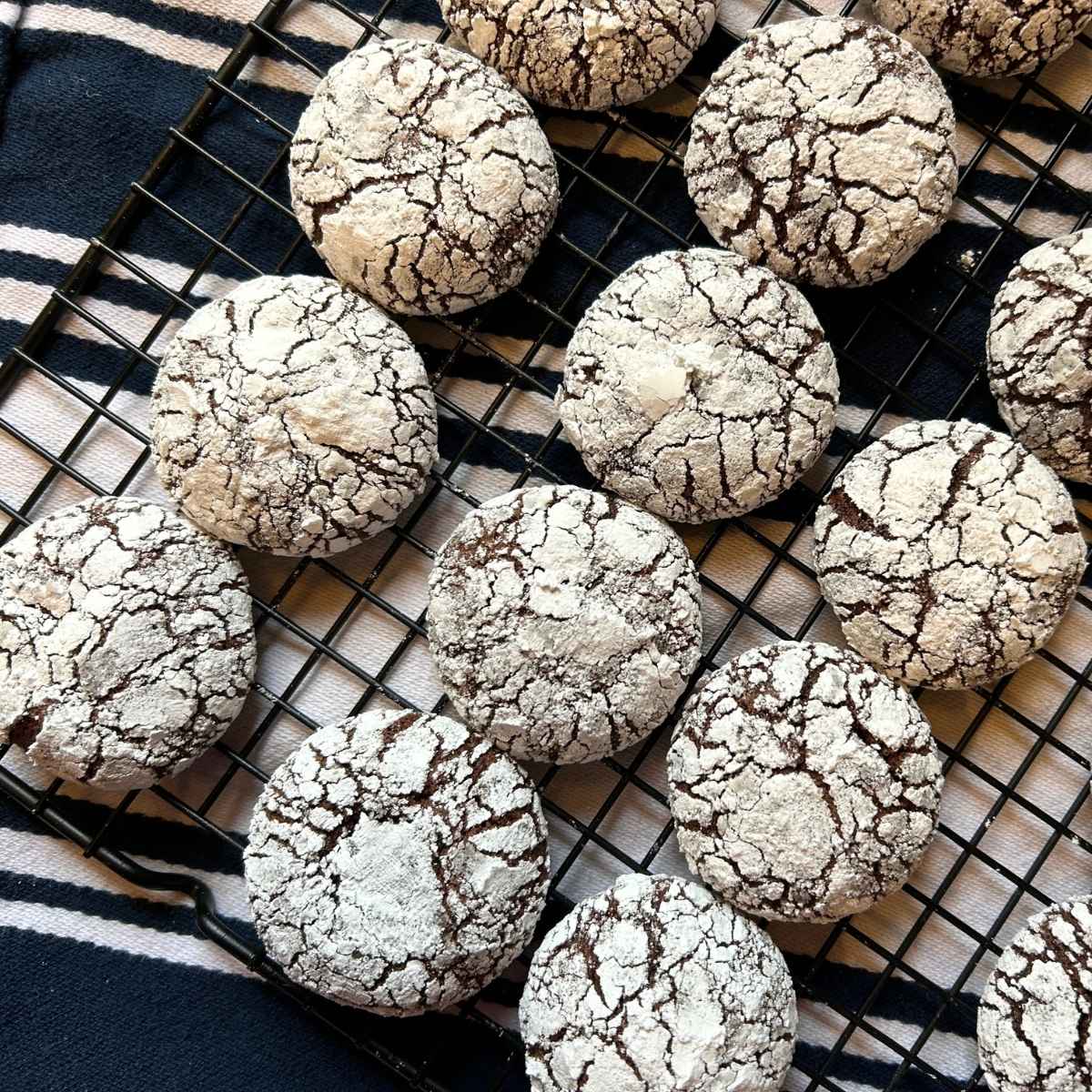 sourdough chocolate crinkle cookies on a cooking rack on top of a navy and white striped towel