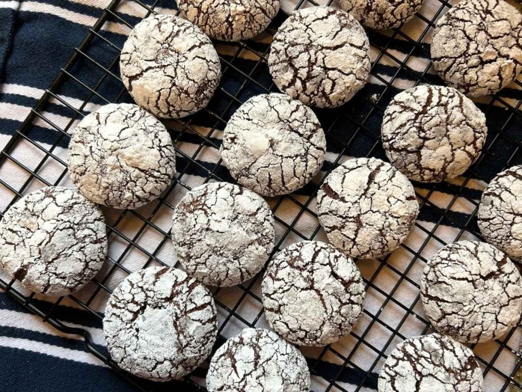 sourdough chocolate crinkle cookies on a cooking rack on top of a navy and white striped towel