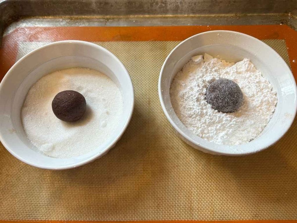 chocolate cookie dough being rolled in granulated sugar and then in powdered sugar