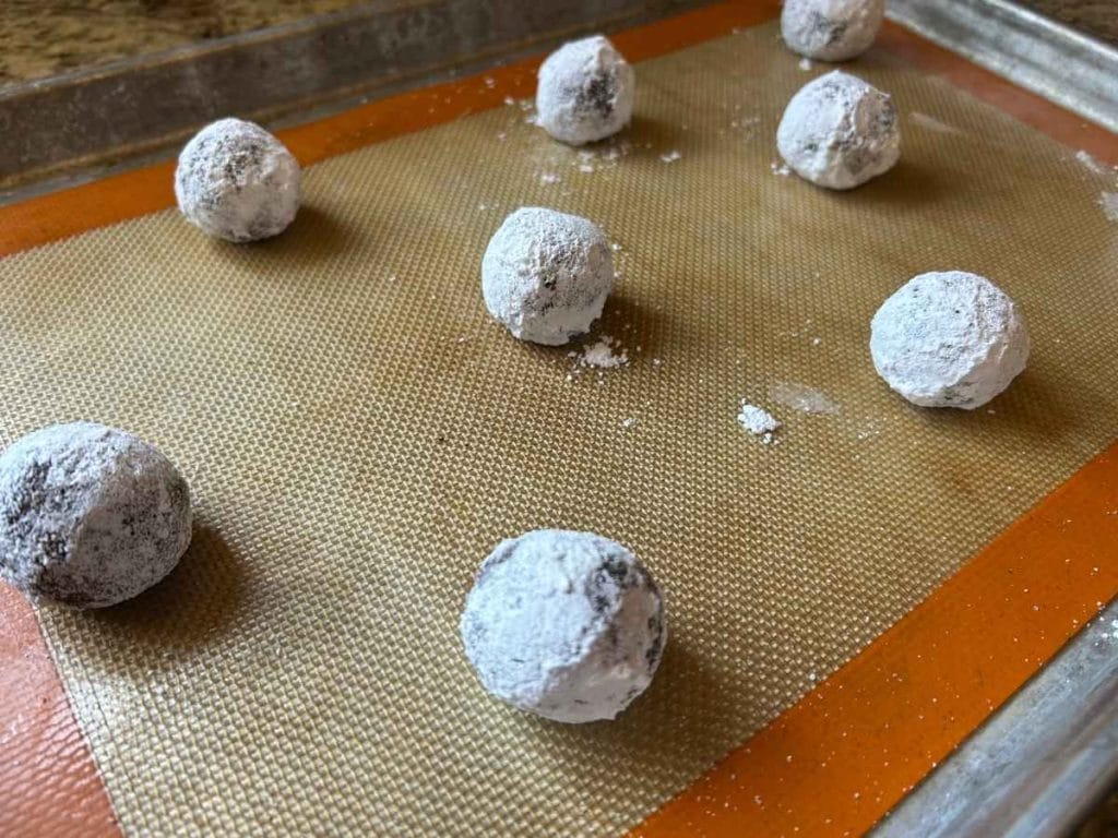 dough balls rolled in powdered sugar on a baking tray