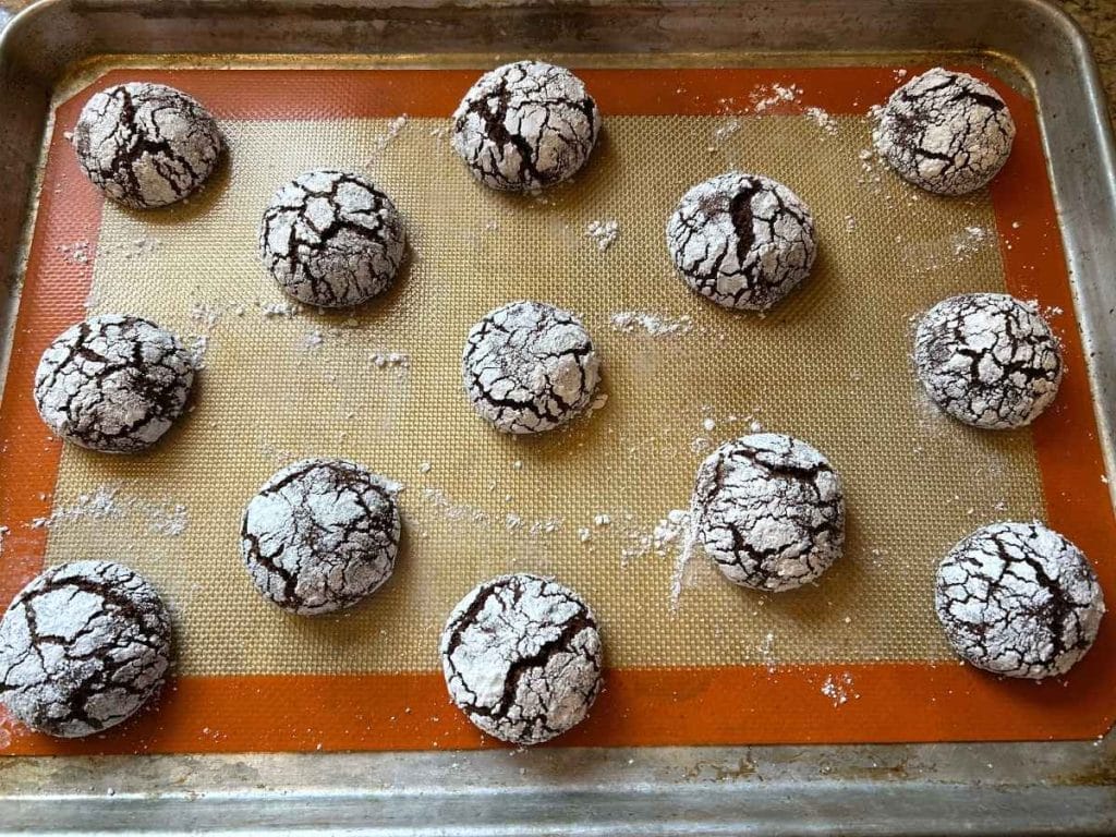 a batch of baked sourdough chocolate crinkle cookies on a baking tray