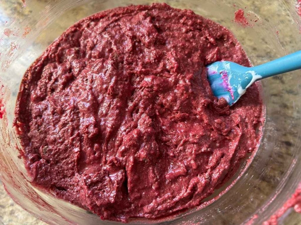 dark pink muffin batter in a glass bowl with a blue spatula