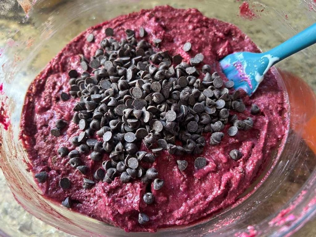 chocolate beet muffin batter with chocolate chips on top in a glass bowl with a blue spatula