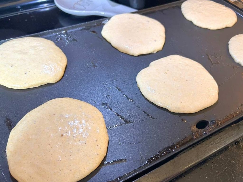 pancake batter on a black electric griddle cooking