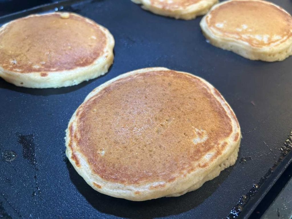 pancakes cooking on their second side on a black electric griddle
