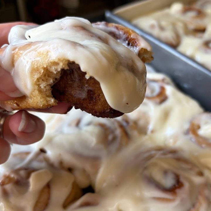 holding one warm cinnamon roll over the pan of the batch