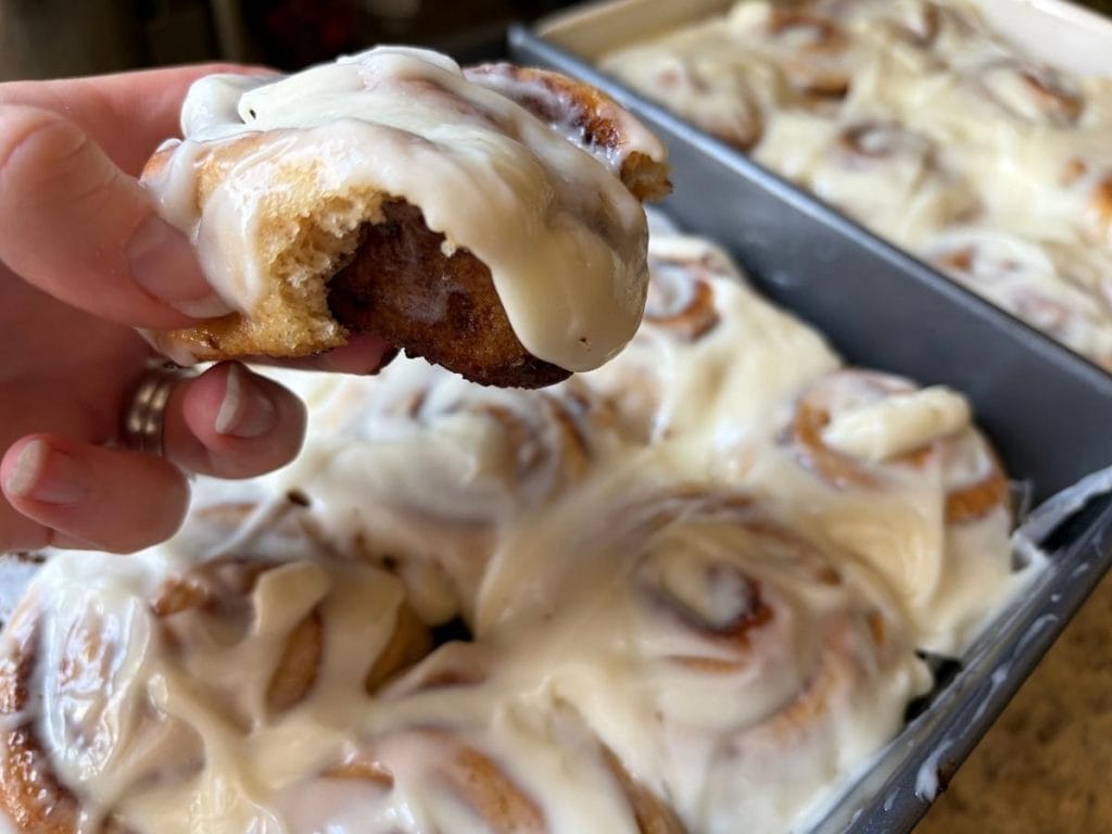holding one warm cinnamon roll over the pan of the batch
