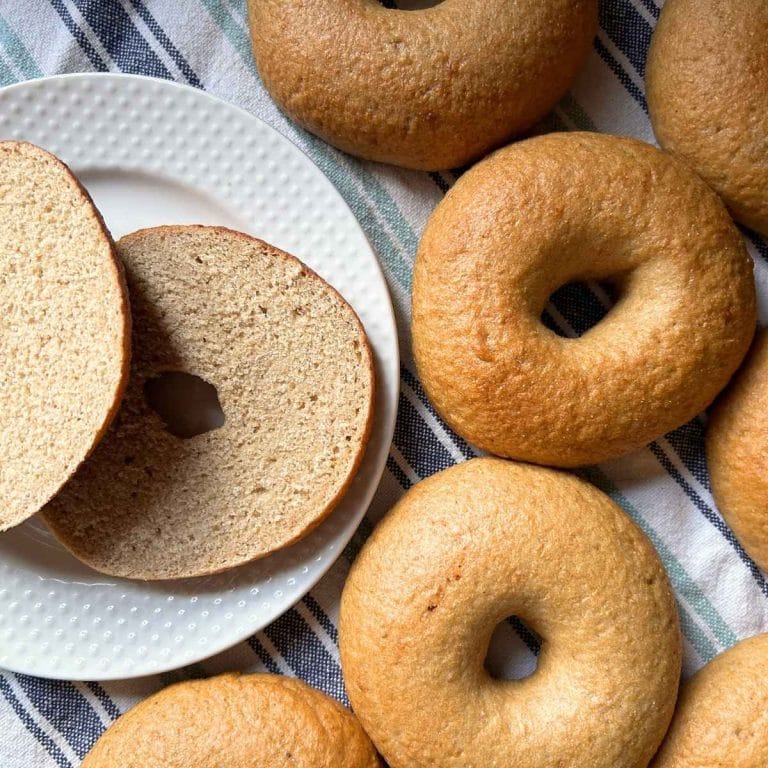 a cut bagel on a plate next to the rest of the batch of sourdough bagels on a striped kitchen towel