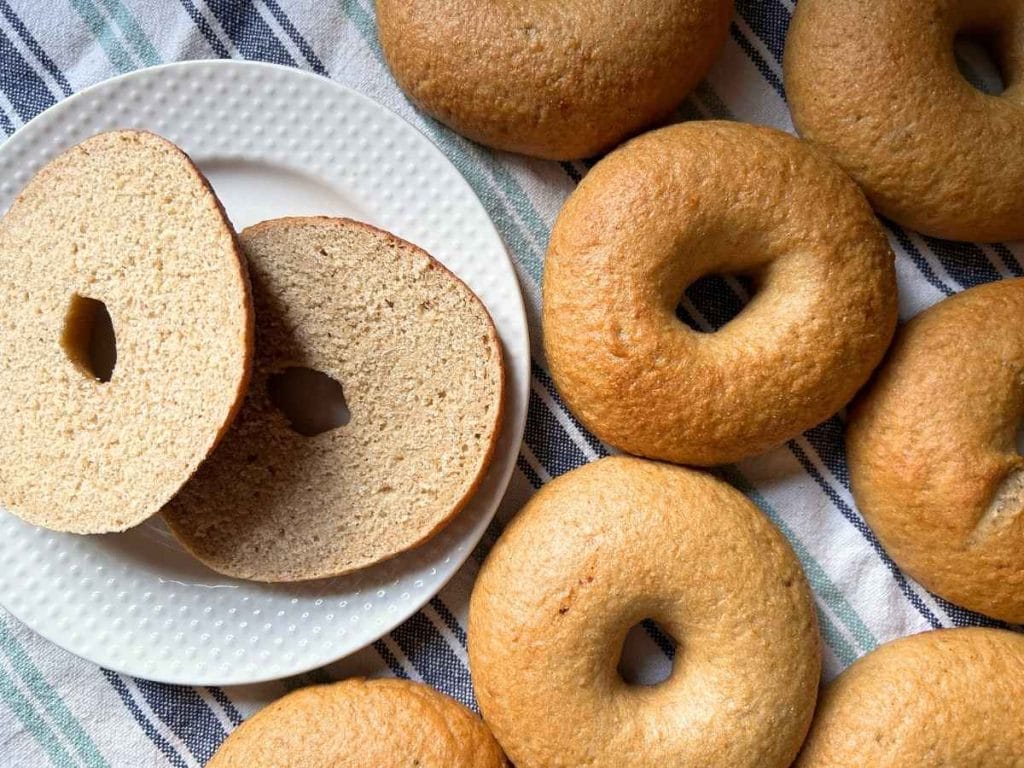 a cut bagel on a plate next to the rest of the batch of sourdough bagels on a striped kitchen towel
