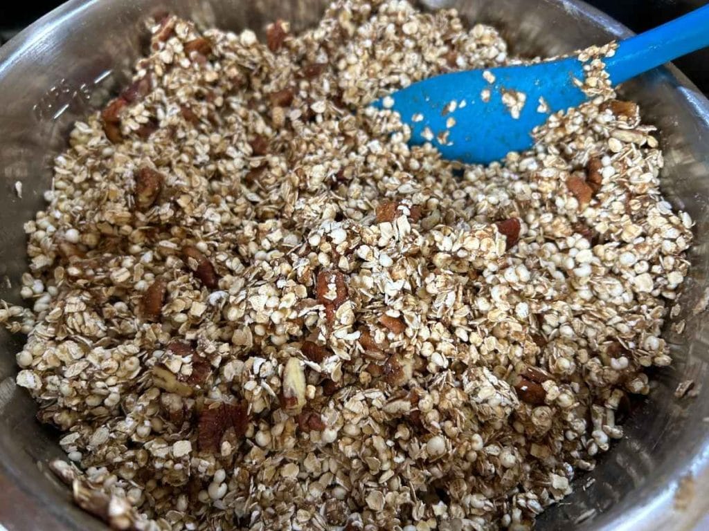 mixing ingredients for granola with a blue spatula in a metal mixing bowl