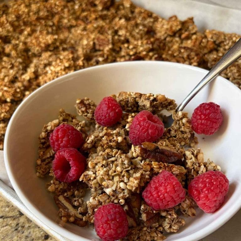 homemade sourdough maple nut granola in a bowl with raspberries next to the pan with the rest of the batch