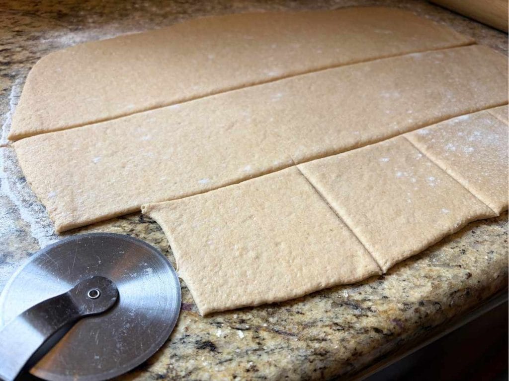 dough rolled out on a counter with some squares cut out using a pizza cutter