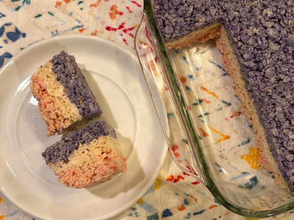 two cut squares of red white and blue rice krispies treats on a plate next to the pan