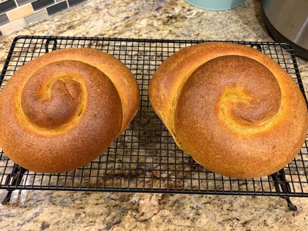 two loaves of baked pumpkin challah bread on a cooling rack