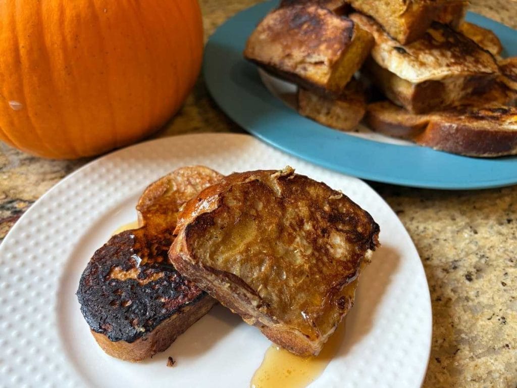 plate of slices pumpkin challah french toast in front of a stack of the rest of the batch next to a pumpkin