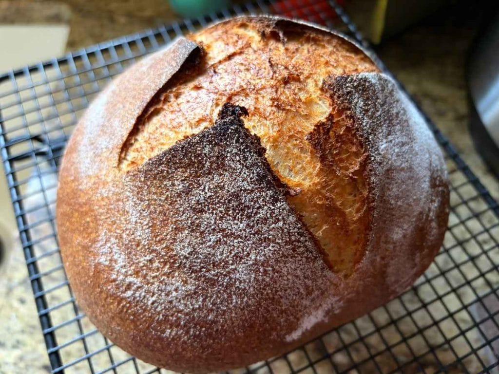 loaf of sourdough bread with an x scored on top sitting on a cooling rack