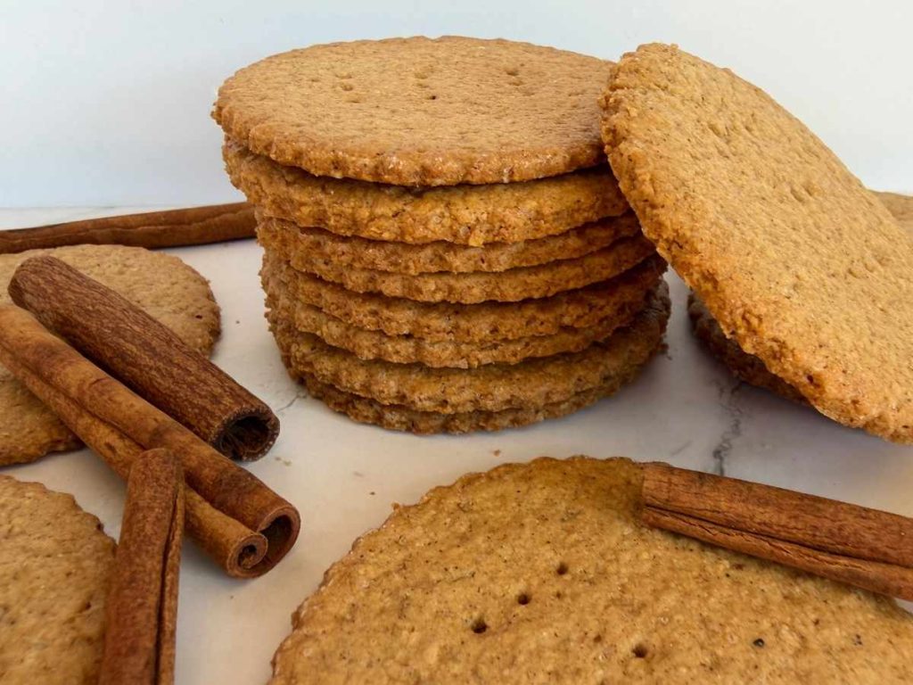 stack of thin, crispy cookies next to cinnamon sticks